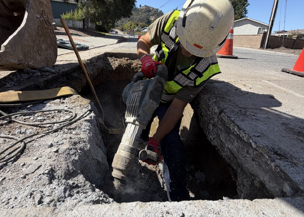 A construction worker using a jackhammer to drill a hole in asphalt